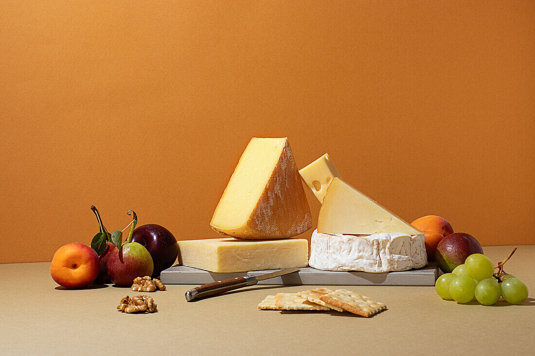 Various cheeses accompanied by fresh fruits including apples, grapes, and apricots assembled elegantly on a beige surface