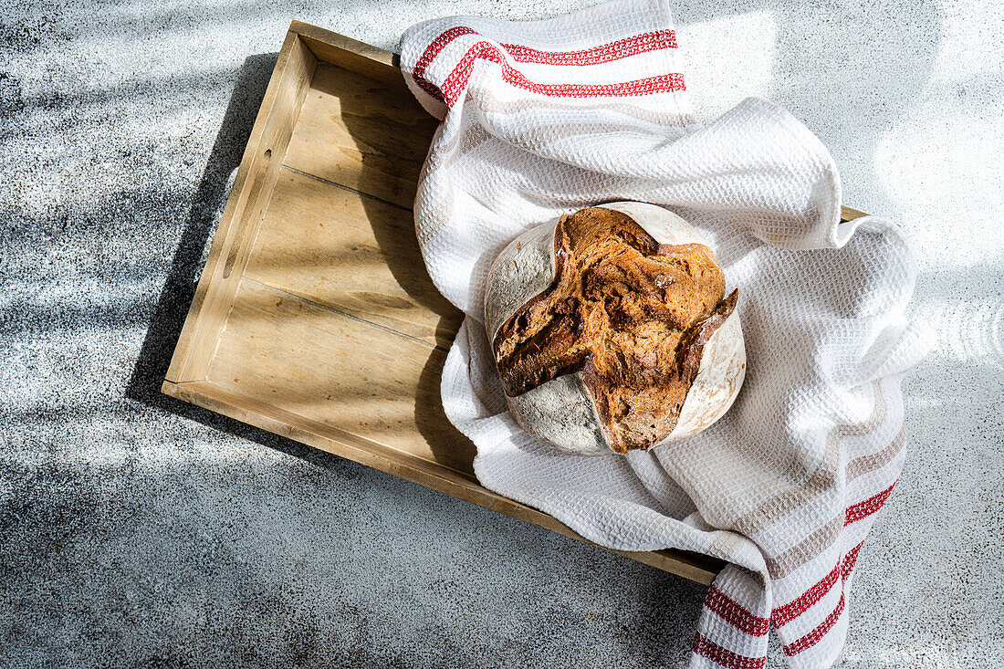 Artisanal sourdough rye bread wrapped in a towel, resting on a wooden tray with a textured background