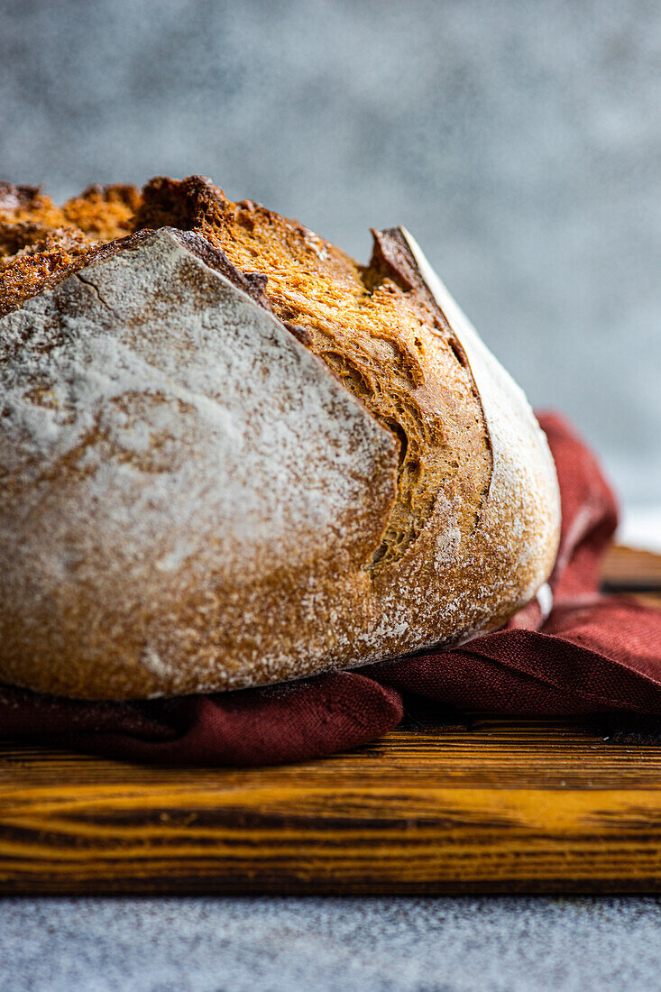 A close-up of a crusty artisan sourdough loaf made with wholesome rye flour, resting on a rustic wooden board with a burgundy cloth