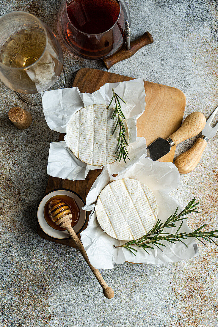 Draufsicht auf ein elegantes Arrangement von Brie-Käse, begleitet von Honig, frischem Rosmarin und Gläsern mit Weiß- und Rotwein.