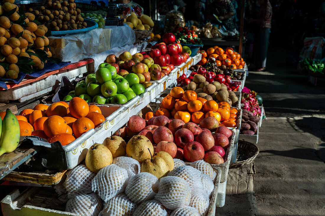 A colorful selection of fresh fruits including green apples, oranges, and pears neatly arranged in crates at a bustling market in Hong Kong.