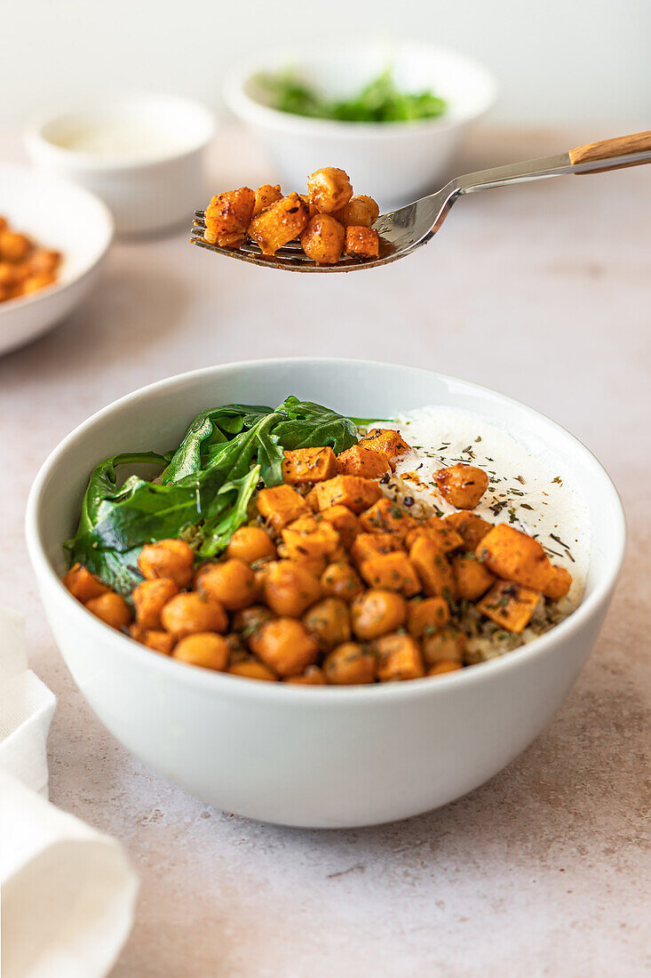 A nourishing bowl of quinoa salad with roasted spiced chickpeas, tender sweet potato chunks, fresh spinach, and a creamy yogurt sauce