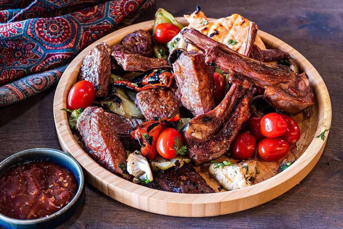 Eine Auswahl an saftigem, gegrilltem Fleisch, darunter Rippchen und Steak, ergänzt durch frische Kirschtomaten und gegrilltes Gemüse, serviert auf einer rustikalen Holzplatte