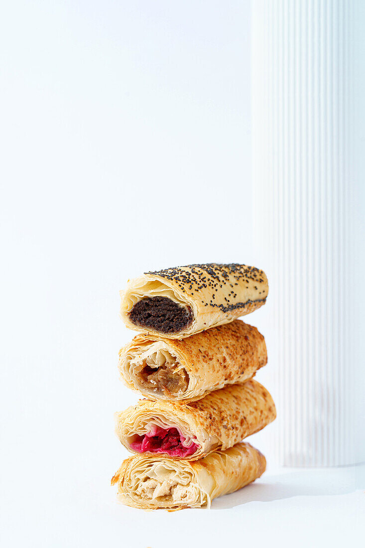 Stacked savory and sweet puff pastries with various fillings displayed against a white background.