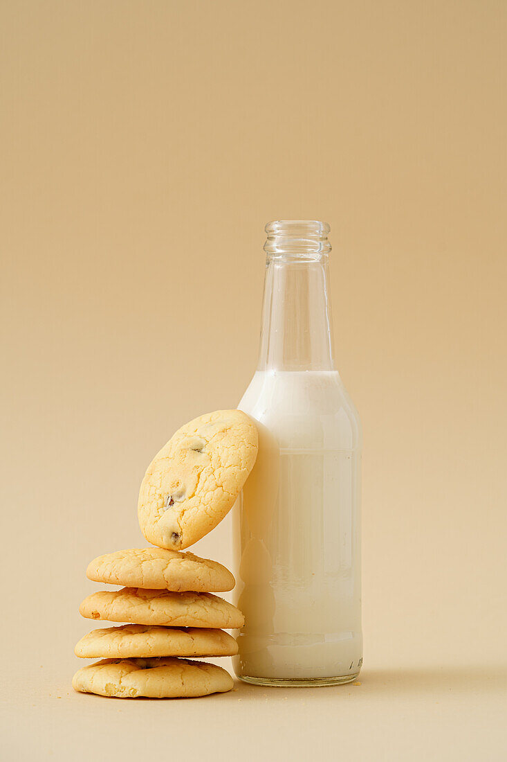 Köstlicher Stapel hausgemachter Rosinenkekse mit einer frischen Flasche Milch auf einem beigen Hintergrund, der einen gemütlichen Snack illustriert.