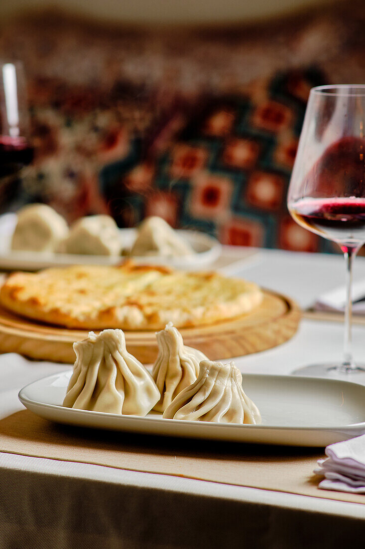 Ein wunderschön komponiertes Bild, das die traditionellen georgischen Gerichte Khinkali und Khachapuri zeigt, die elegant auf einem Restauranttisch serviert werden, begleitet von einem Glas Rotwein