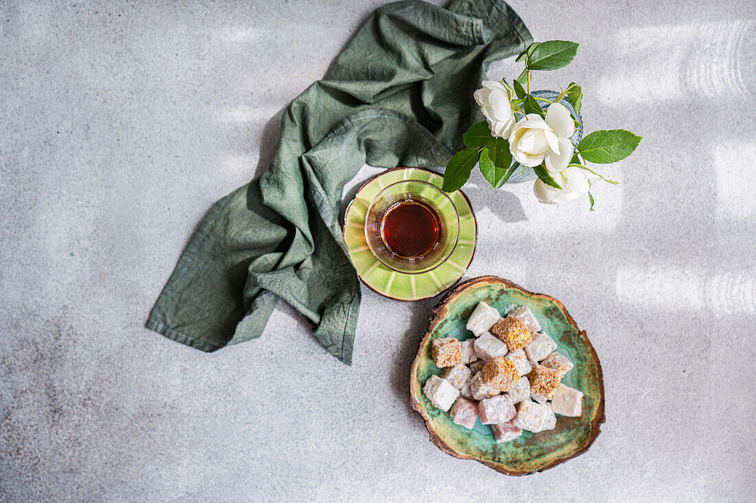 An assortment of traditional Turkish delights served with black tea, accompanied by a vase of beautiful white roses