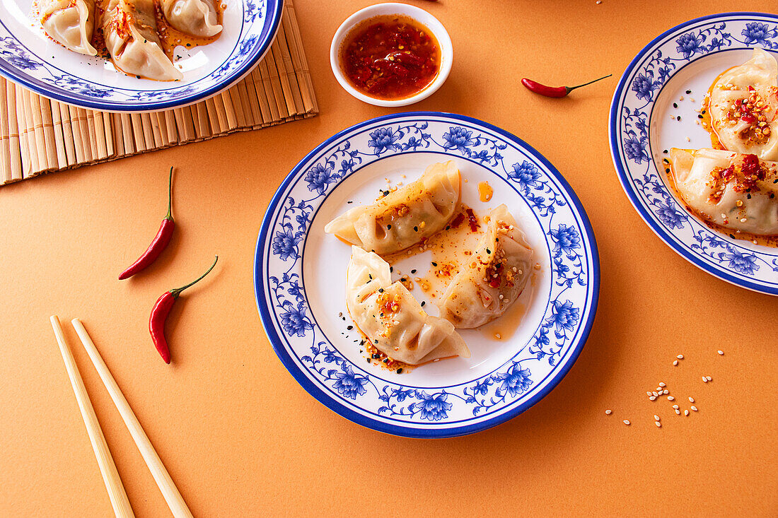 Overhead view of traditional Asian dumplings served on ornate blue and white plates, complemented by a spicy dipping sauce and red chili peppers