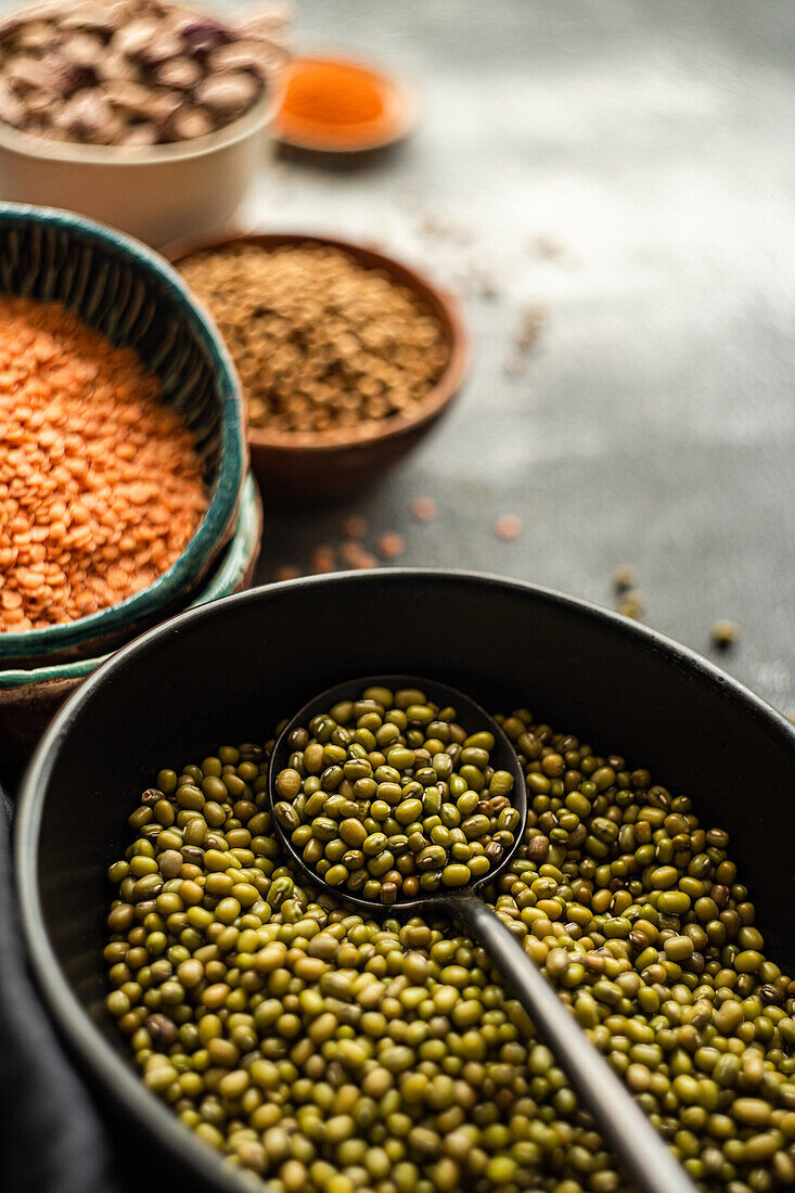 Variety of colorful organic beans including mung, lentils, and chickpeas showcased in rustic kitchenware Ideal for health and culinary themes