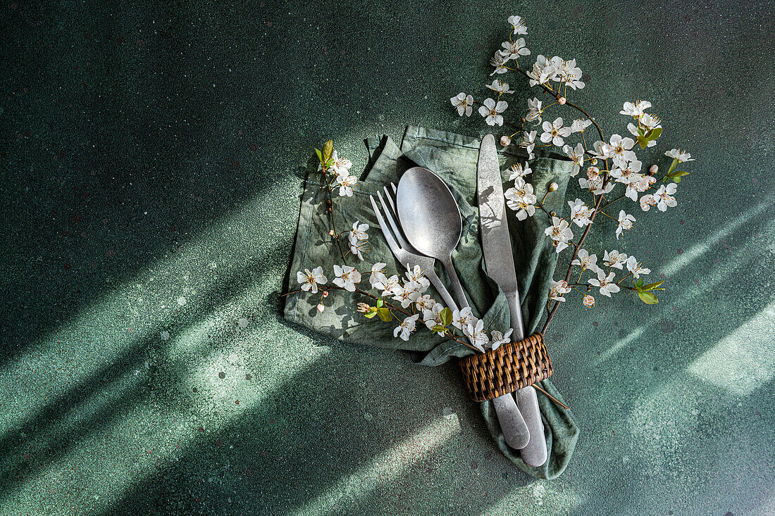 Eleganter Löffel, Gabel und Messer, zusammengebunden auf einer grünen Serviette mit Kirschblüten