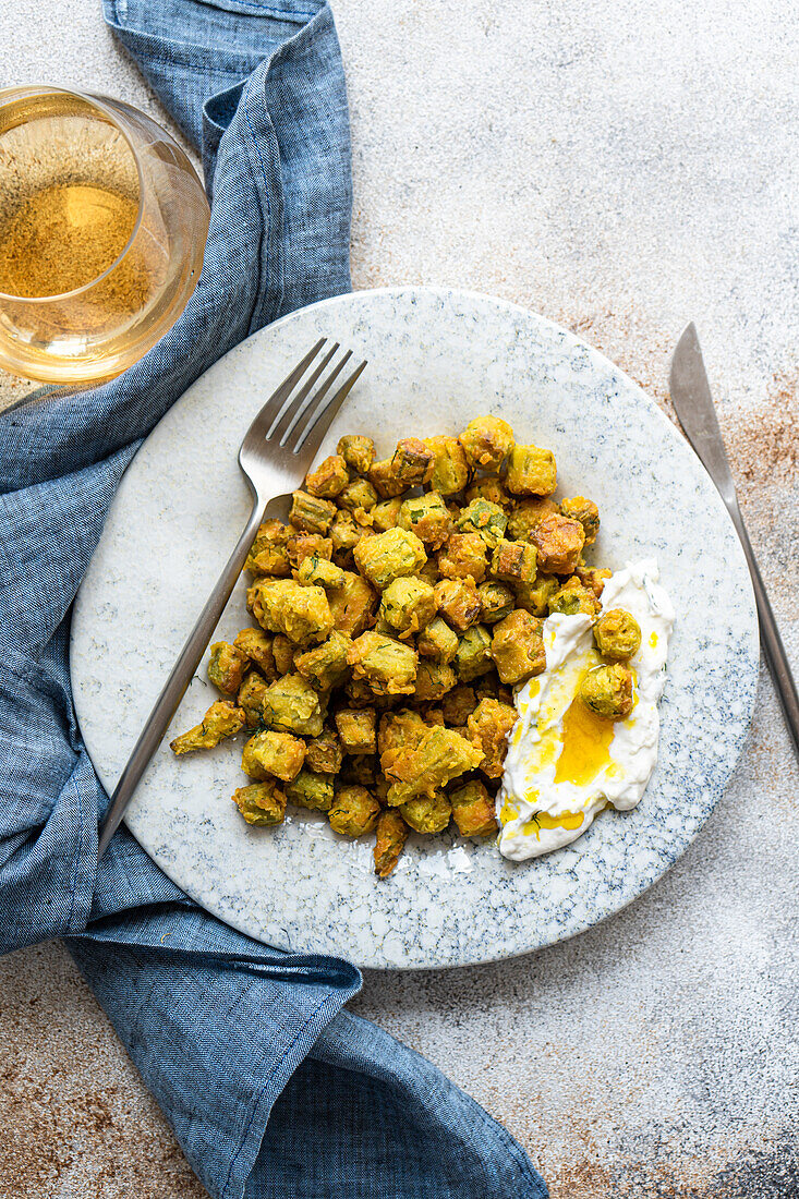 Gebratene Bamia, serviert auf einem gesprenkelten Keramikteller, begleitet von einer Dill-Knoblauch-Sauerrahmsauce, ein traditionelles mediterranes Gericht