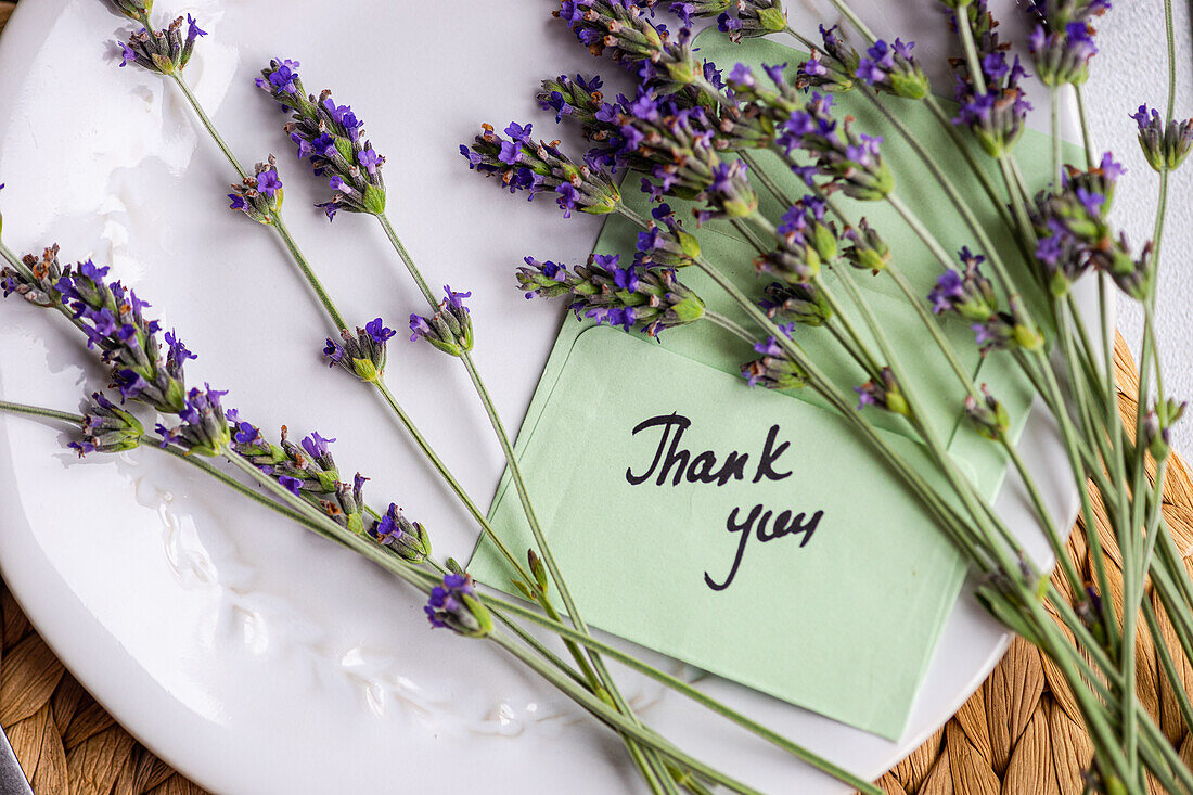 An inviting summer table setting featuring fresh lavender flowers and a thoughtful thank you card atop a white plate, exuding a sense of gratitude and seasonal charm