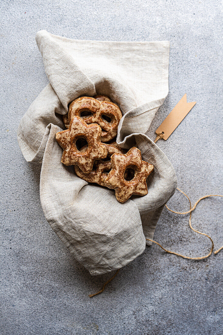 Top view of homemade gingerbread cookies shaped like stars, nestled in a gray linen pouch with a rustic tag on a textured surface.