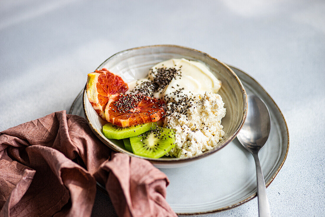 A nutritious breakfast bowl featuring creamy cottage cheese, natural yogurt, chia seeds, fresh kiwi slices, and a juicy wedge of Sicilian orange