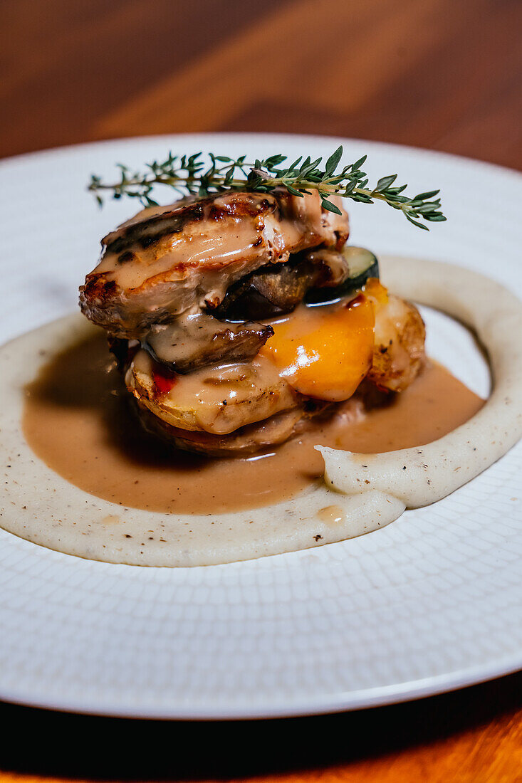 Layered chicken medallions paired with zucchini and bell pepper, topped with a creamy sauce and fresh thyme, presented on a textured white plate