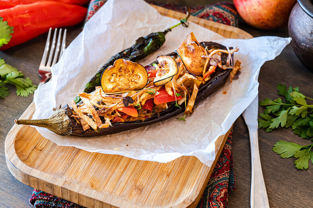 From above, a stuffed eggplant with slices of cherry tomatoes, bell pepper, onion, garlic, and potatoes, topped with melted cheese and served with microgreens.