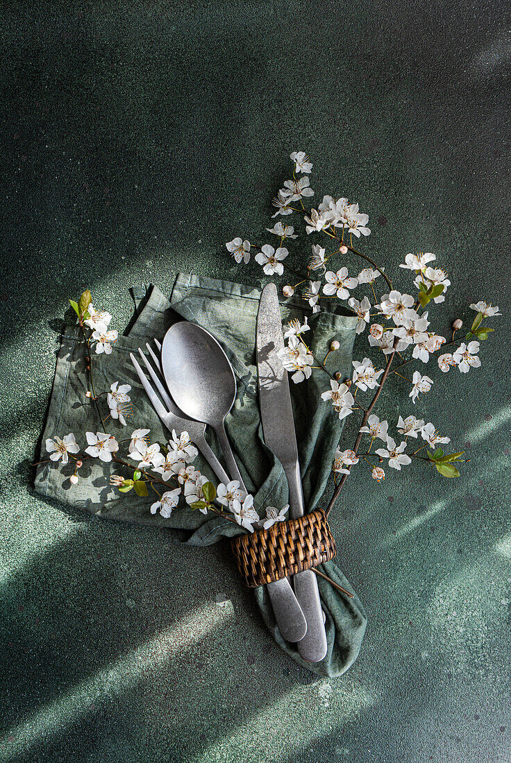 Cutlery is wrapped in a green napkin with cherry blossoms, set on a textured background