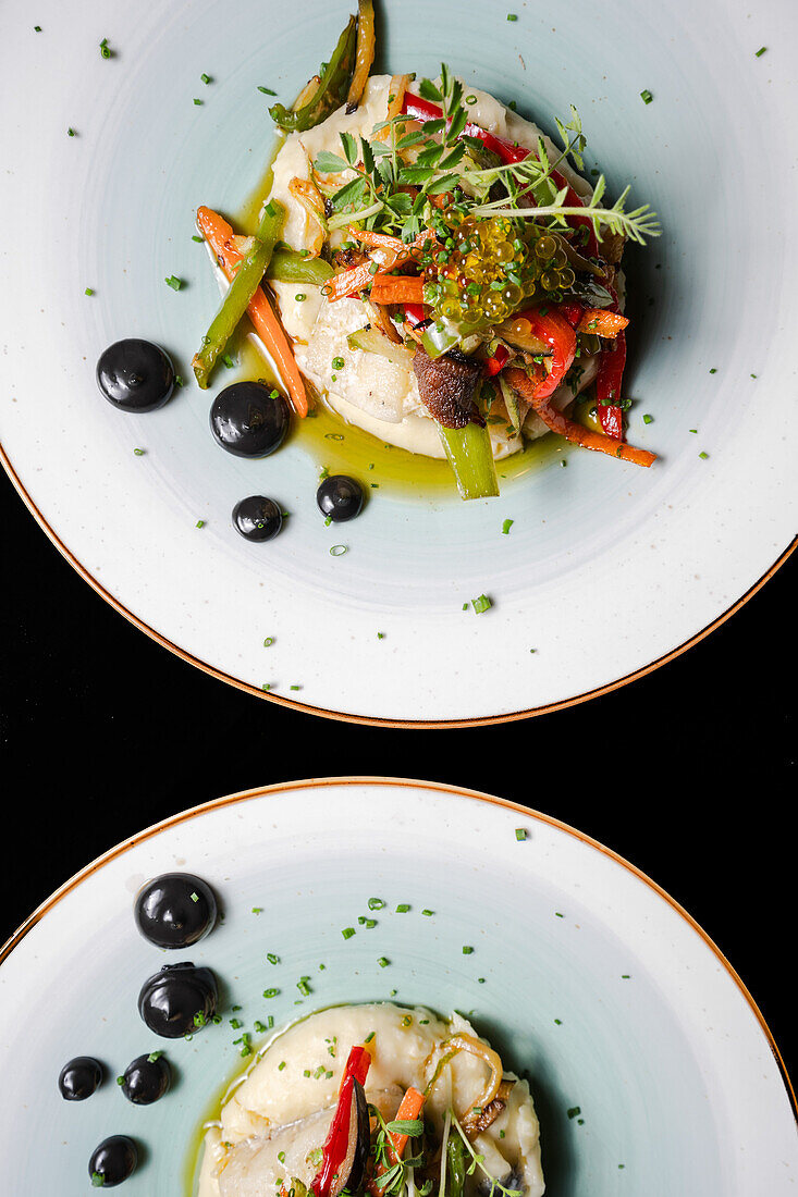 Top view of exquisite cod confit placed on a smooth mashed potato base, topped with colorful sauteed vegetables, garnished with fresh chives and drizzled with infused olive oil.