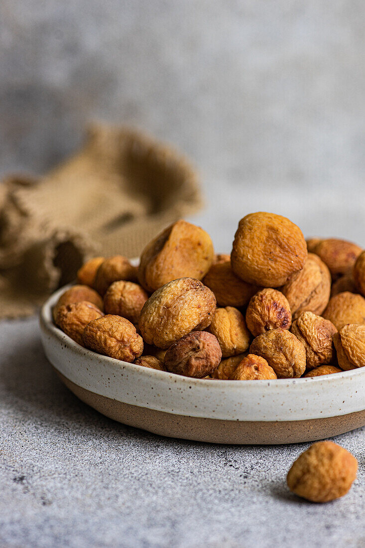 A bowl of Arashan Kandak, Central Asian wild apricots sun-dried for a healthy snack, set on a textured surface with a rustic background