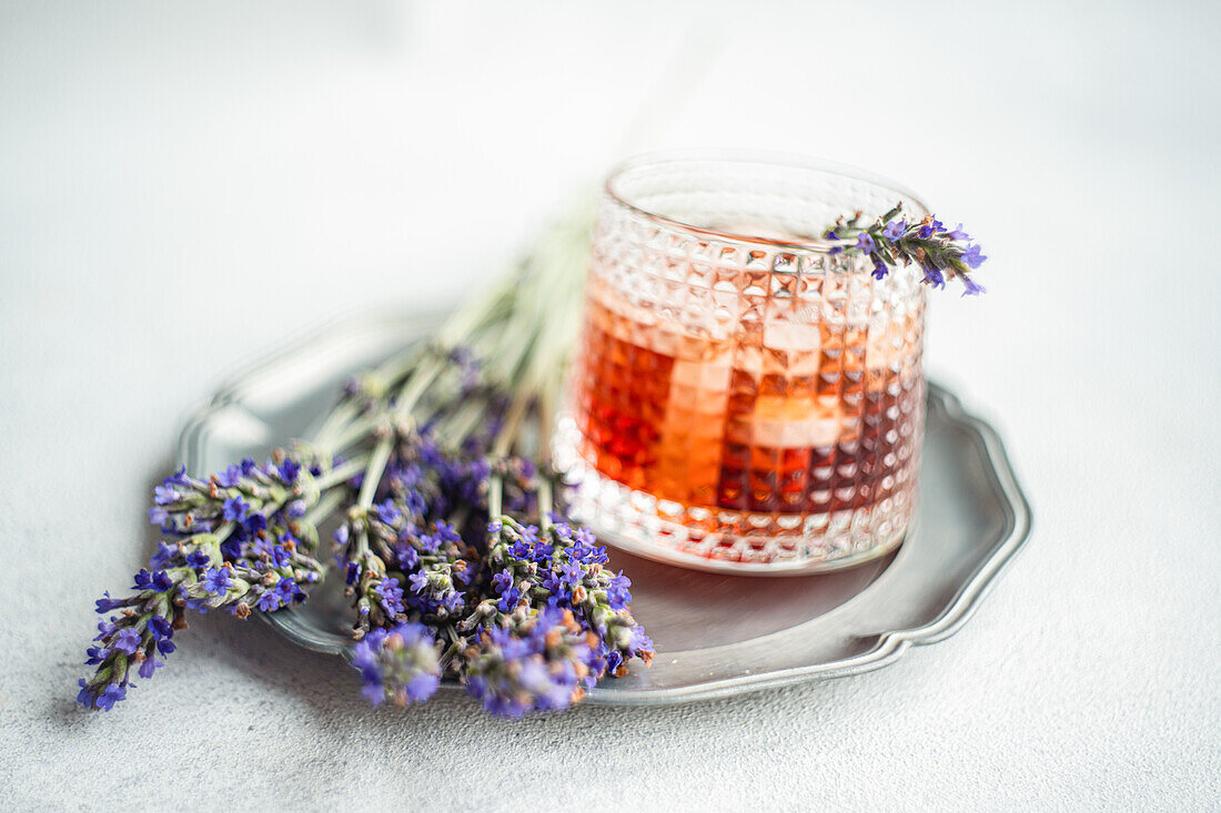 A sophisticated cognac cocktail served in a textured glass, beautifully garnished with fresh lavender sprigs on a silver tray, showcasing a blend of rustic charm and luxury