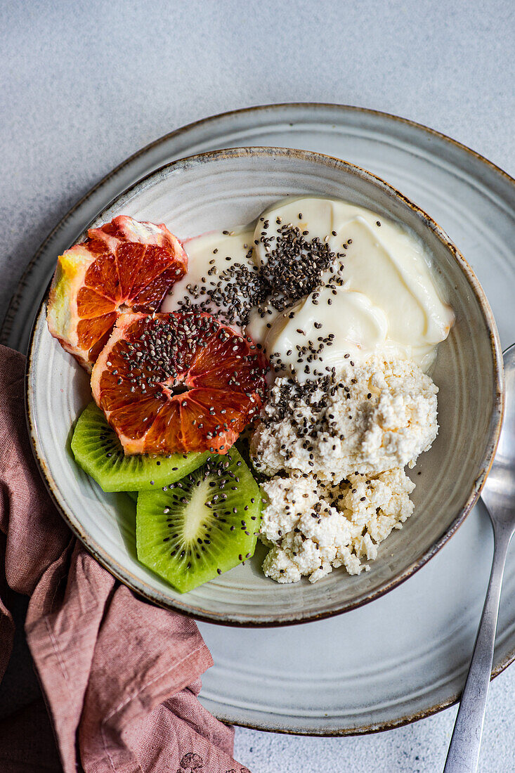 Top view of nutritious breakfast bowl featuring creamy cottage cheese, natural yogurt, chia seeds, fresh kiwi slices, and a juicy wedge of Sicilian orange