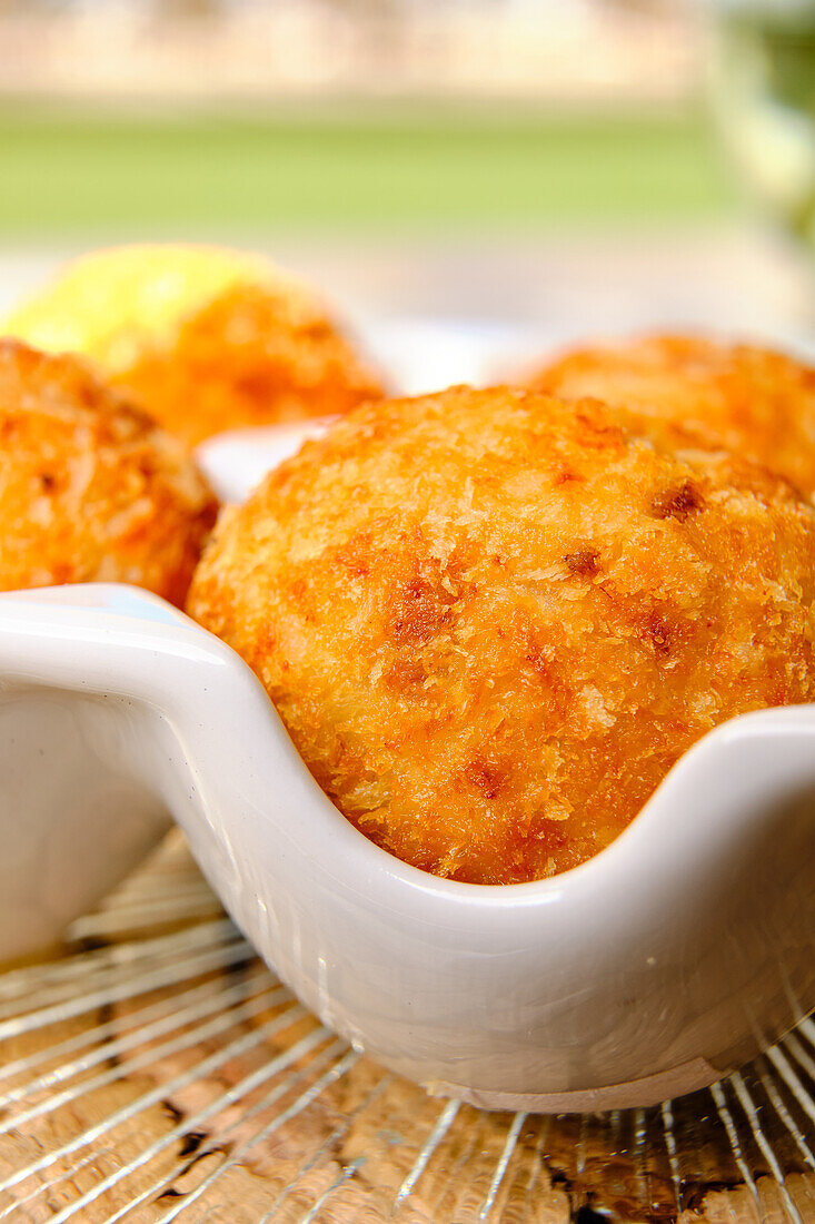 A delicious close-up view of golden brown arancini, traditional Italian rice balls, served in a white ceramic bowl on a rustic background, showcasing their crispy texture and tempting appearance.