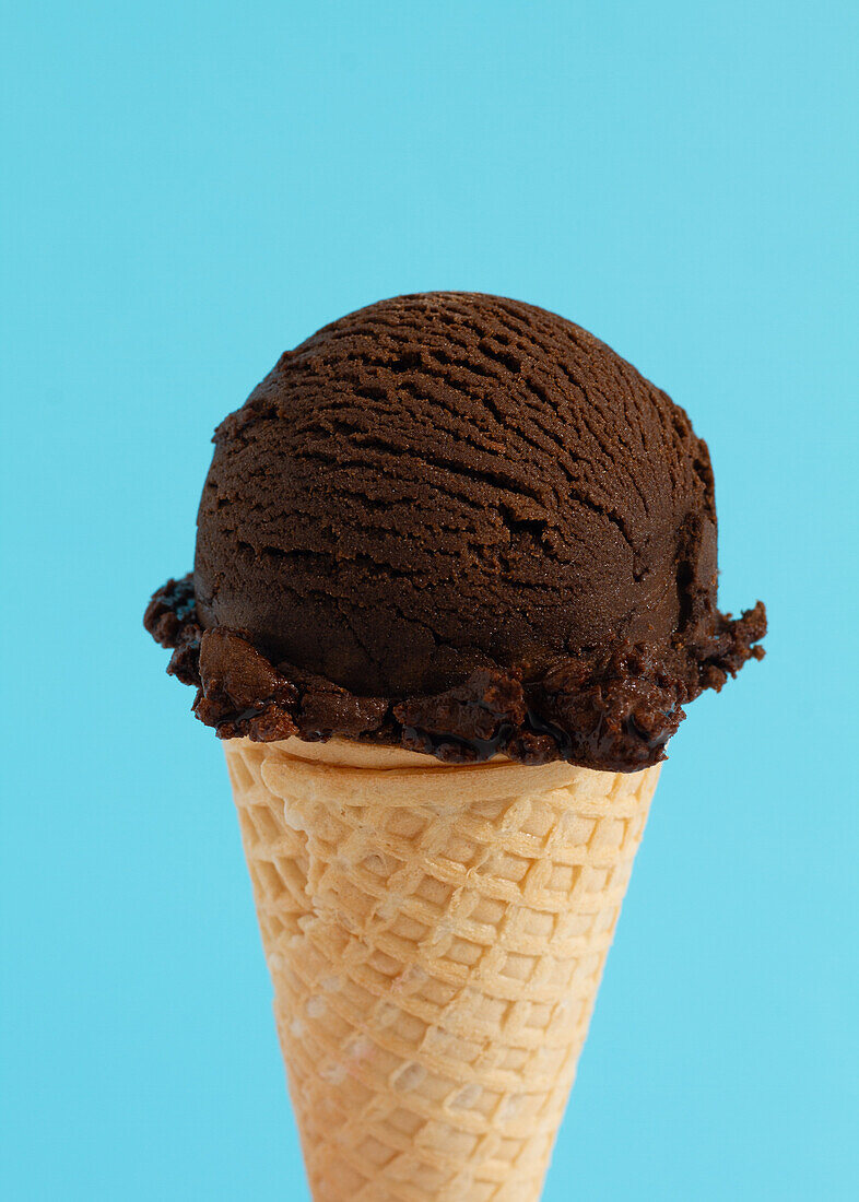 Scoop of chocolate ice cream in a waffle cone in blue background