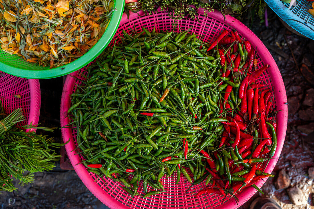 Blick von oben auf leuchtend rote und grüne Chilis in farbenfrohen Körben auf einem lokalen Markt in Kathmandu, auf dem frische Produkte in einer belebten Umgebung angeboten werden.