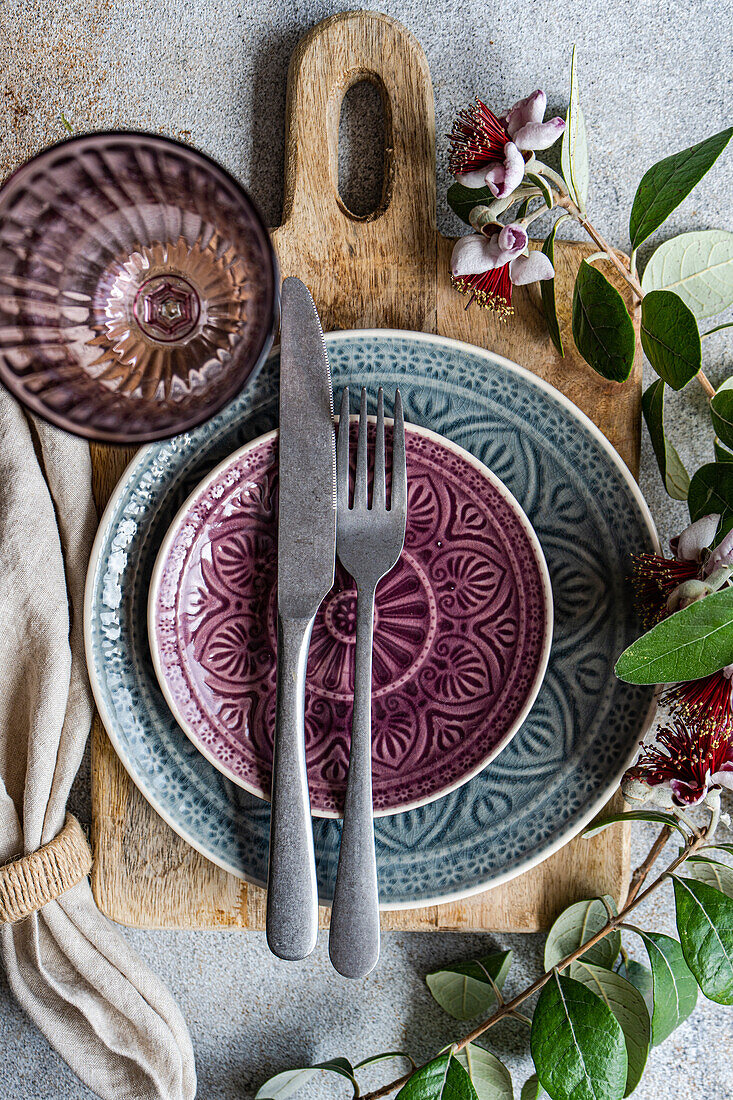 Top view image captures a beautiful table setting featuring a rustic wood cutting board, textured ceramic plates in shades of purple and blue, complemented by a unique feijoa branch as a natural decorative element