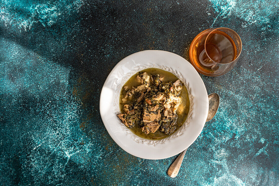 Top view of hearty traditional Georgian dish featuring stewed meat, infused with white wine and seasoned with fresh herbs including tarragon, coriander, parsley, and spring green onions, served with a side of green plums.