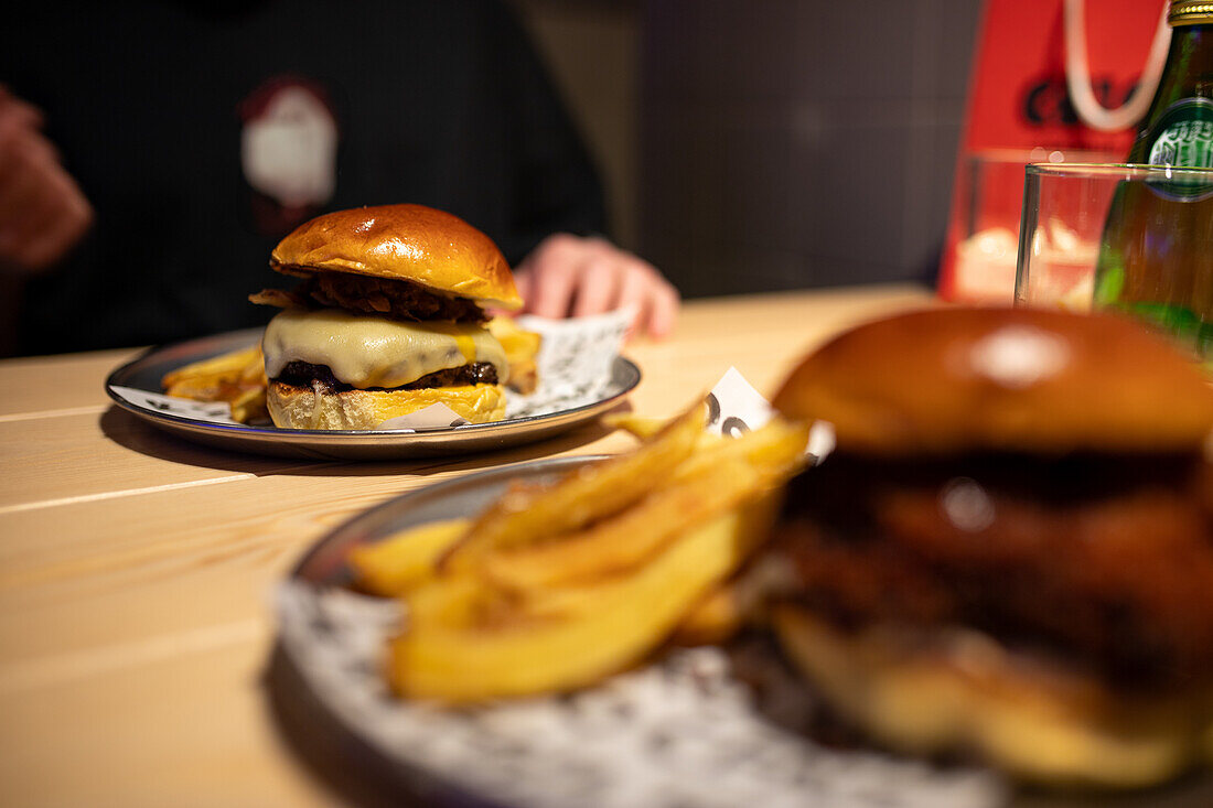 A close-up view of a deliciously juicy cheeseburger topped with melting cheese, paired with a side of golden fries, served on contemporary tableware in a cozy restaurant setting