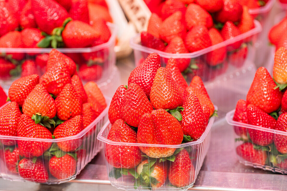 Vibrant strawberries in clear plastic boxes showcased for sale, highlighting freshness and appealing color