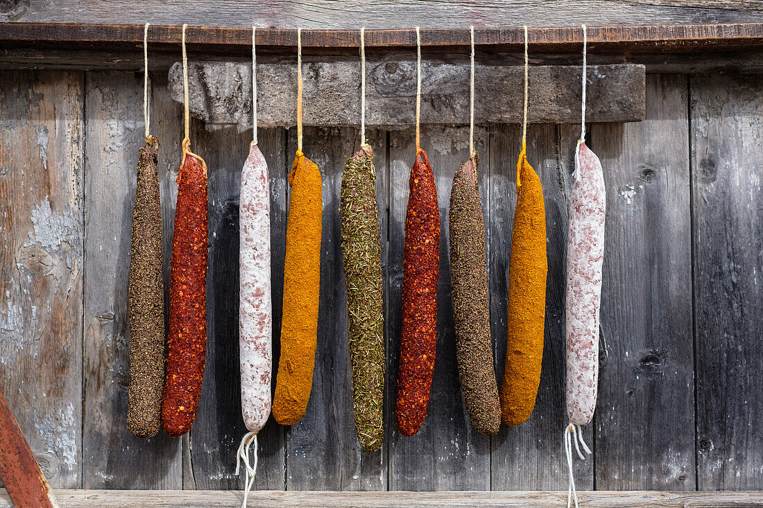 An assortment of vibrant cured sausages including sobrasada, displayed hanging against an aged wooden background, highlighting the rich textures and colors of spices.