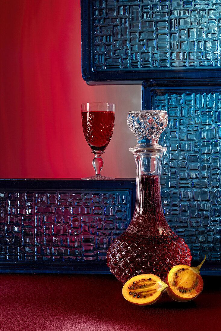 A crystal decanter with rich reddish-brown bitter tamarind beverage, complemented by a matching glass against a red and blue textured backdrop