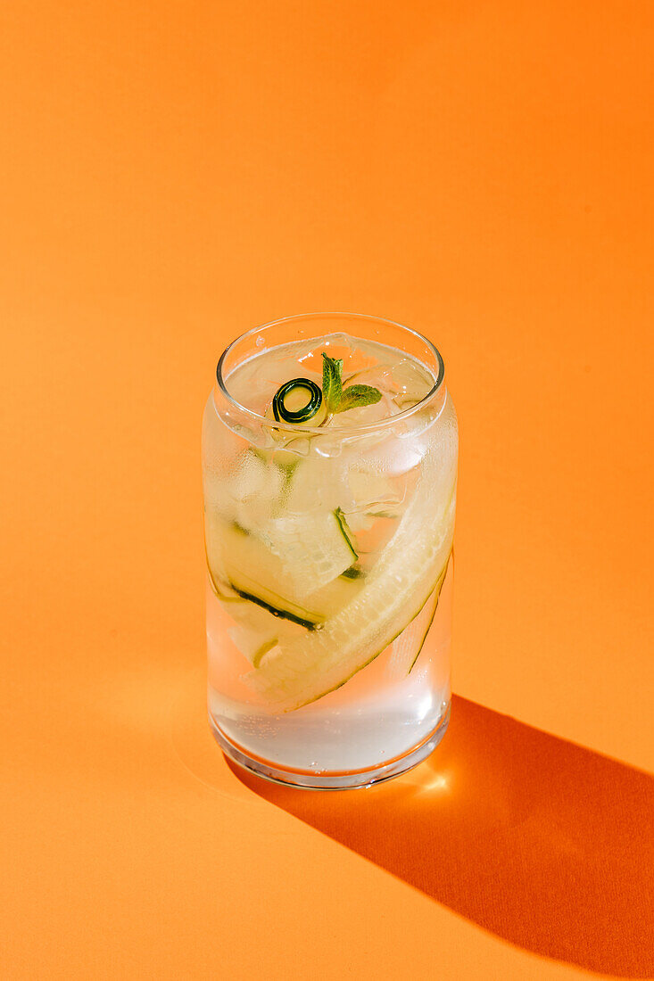 Ein erfrischendes Glas Holunder-Gurken-Limonade mit frischer Minze, serviert auf einem orangefarbenen Hintergrund, perfekt für eine sommerliche Erfrischung.