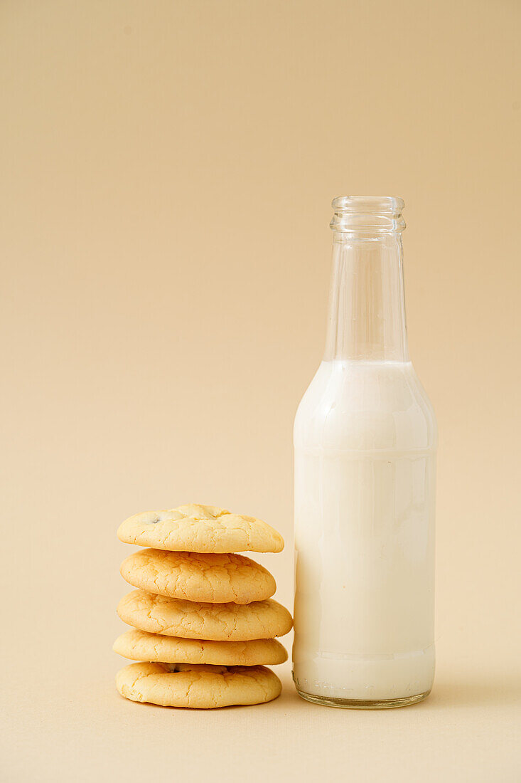 A stack of homemade raisin biscuits beside a full bottle of milk presented against a soft pastel background, invoking a sense of cozy home baking.