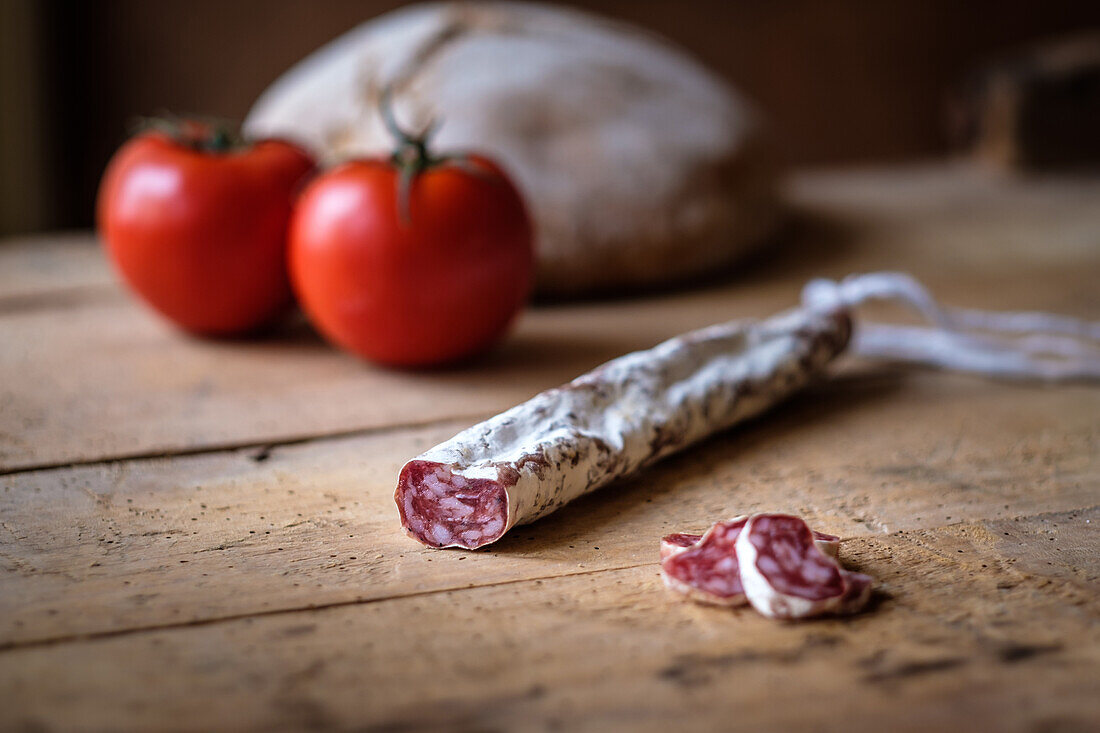 A rustic image featuring sliced cured fuet alongside fresh tomatoes, laid on a rough wooden surface, capturing the essence of traditional culinary delights.