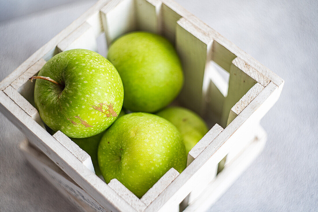 A close-up image showcasing several ripe green apples with a dewy texture, nestled snugly in a rustic white wooden crate, emphasizing freshness and natural beauty