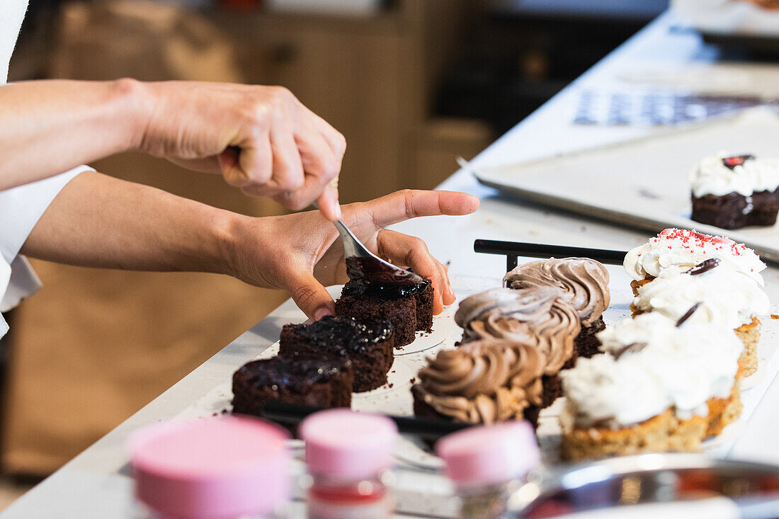 Crop anonymous baker spreading chocolate on vegan sponge cakes while standing at table in bakery and preparing tasty desserts