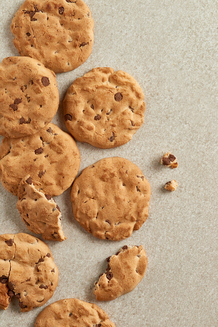 Top view image of chocolate chip cookies with visible bite marks, scattered on a textured backdrop