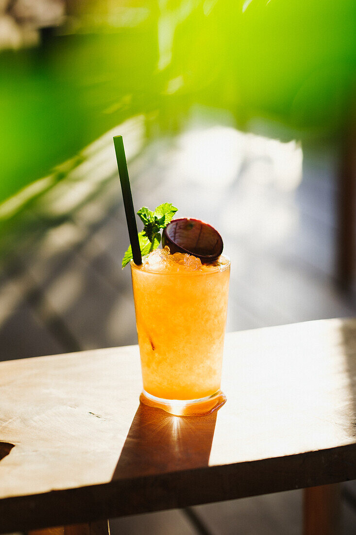 A vibrant summer cocktail adorned with mint on a wooden table, bathed in natural sunlight which accentuates its refreshing look and feel