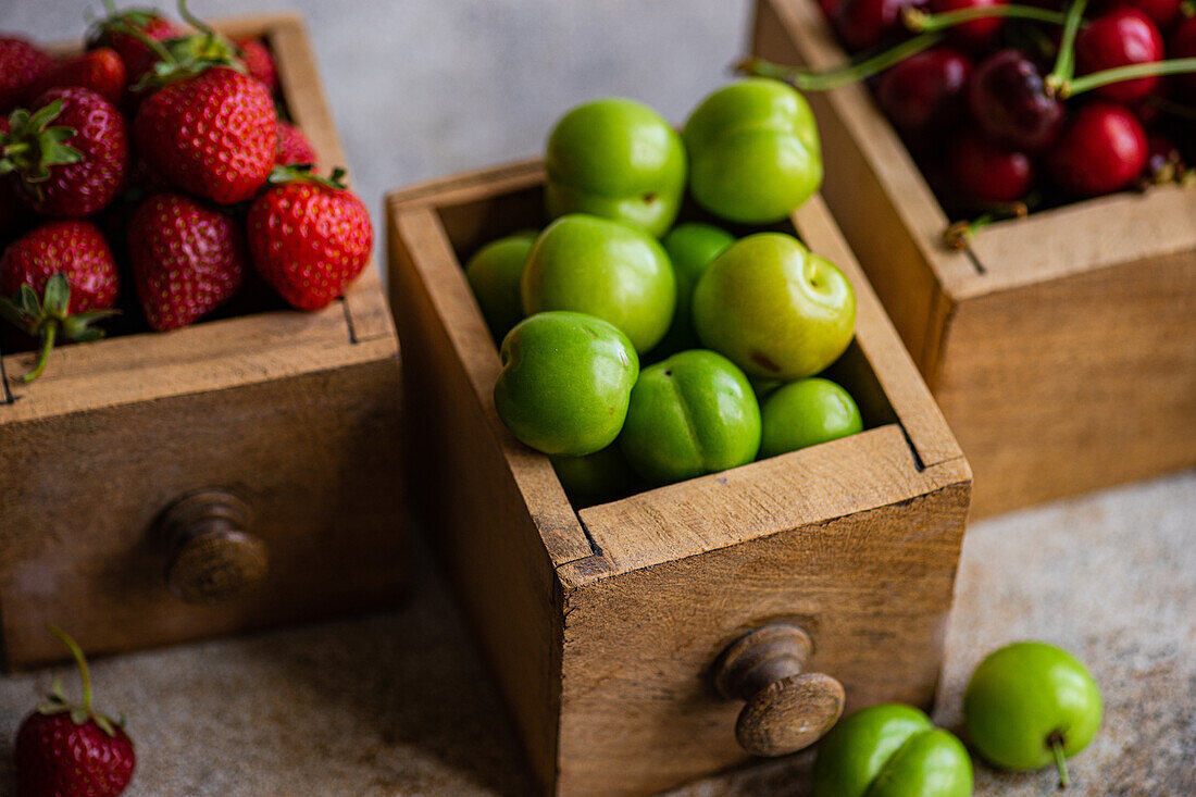 Holzschubladen im Vintage-Stil, gefüllt mit frischen Bio-Erdbeeren, Süßkirschen und grünen Pflaumen, präsentiert in einer rustikalen, natürlichen Umgebung mit dem Schwerpunkt auf gesunden, farmfrischen Produkten