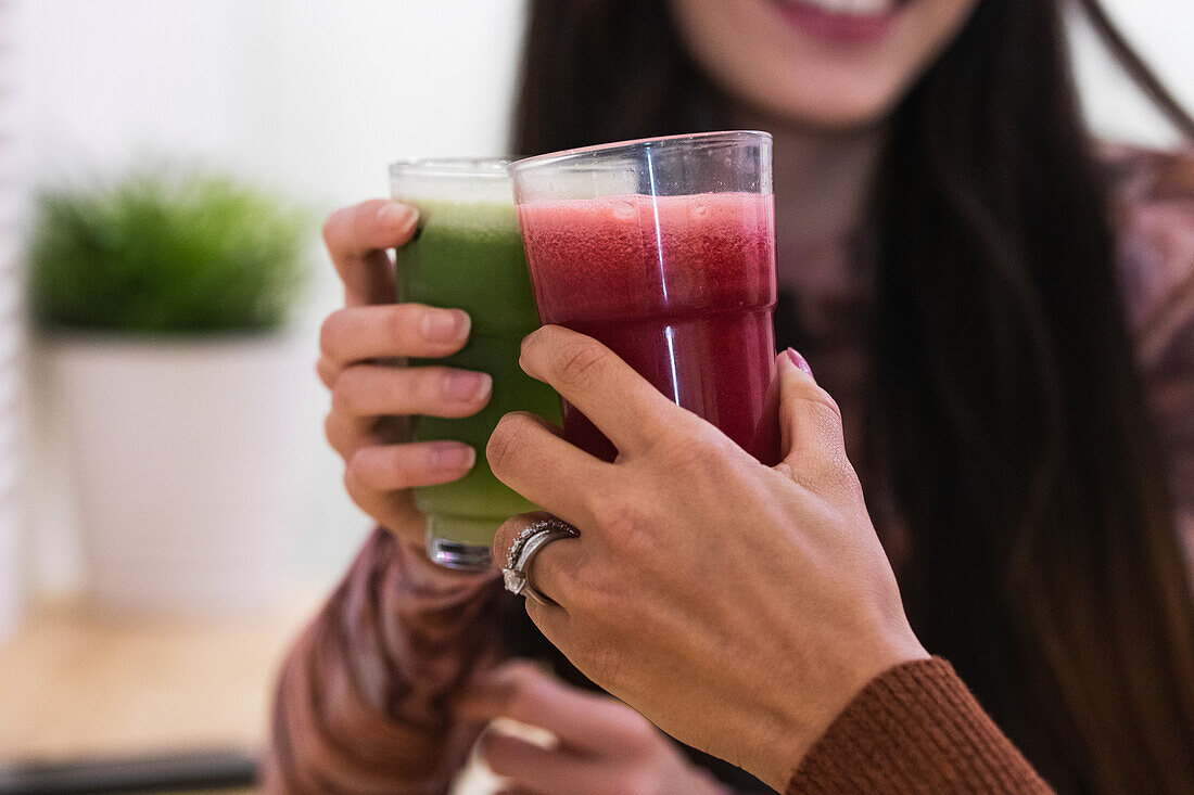 Abgeschnittene, nicht erkennbare, multiethnische Freundinnen sitzen am Tresen und trinken einen erfrischenden Smoothie, während sie in einer Bar chillen