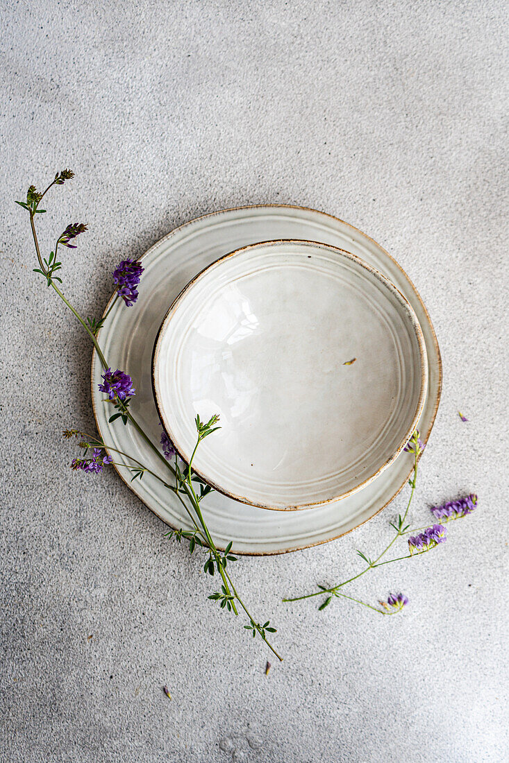 Draufsicht auf einen minimalistisch gedeckten Sommertisch mit einem Vintage-Teller und wilden Alfalfa-Blumen, die einen Hauch von natürlicher Eleganz verleihen.