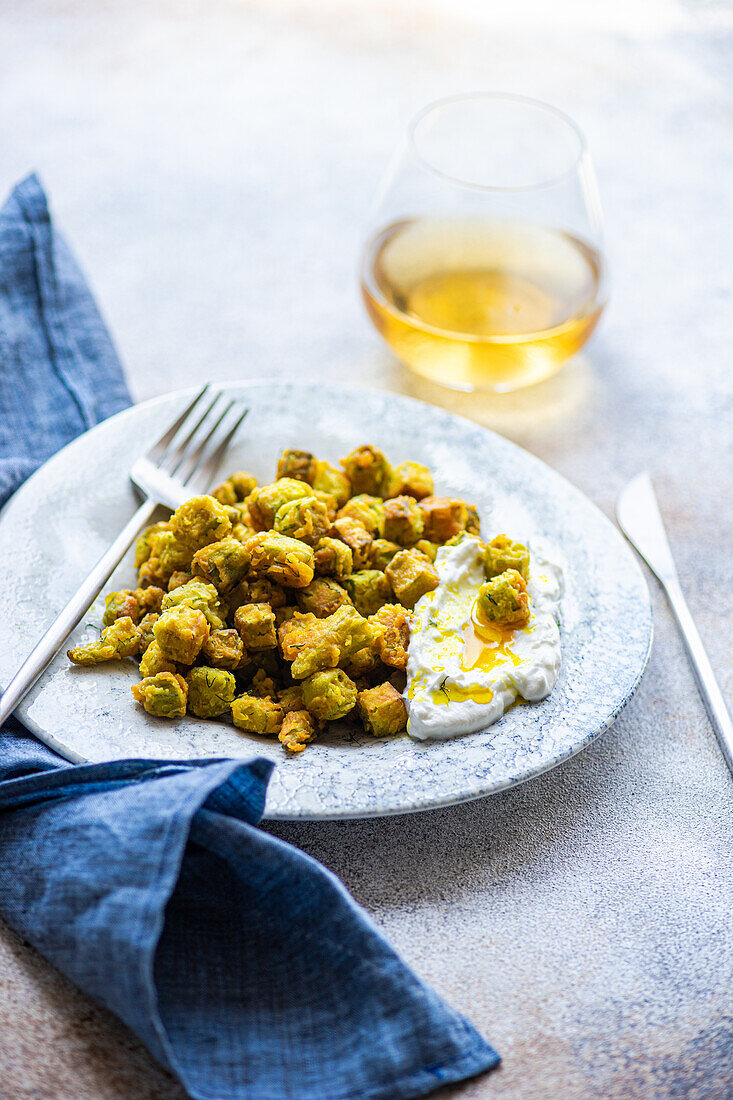 A delectable serving of fried bamia accompanied by a zesty sour cream sauce flavored with dill and garlic, presented on an elegant ceramic plate next to a glass of white wine