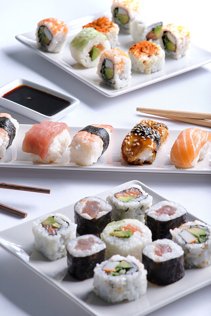 An enticing assortment of sushi rolls neatly arranged on two white plates, accompanied by soy sauce and chopsticks.