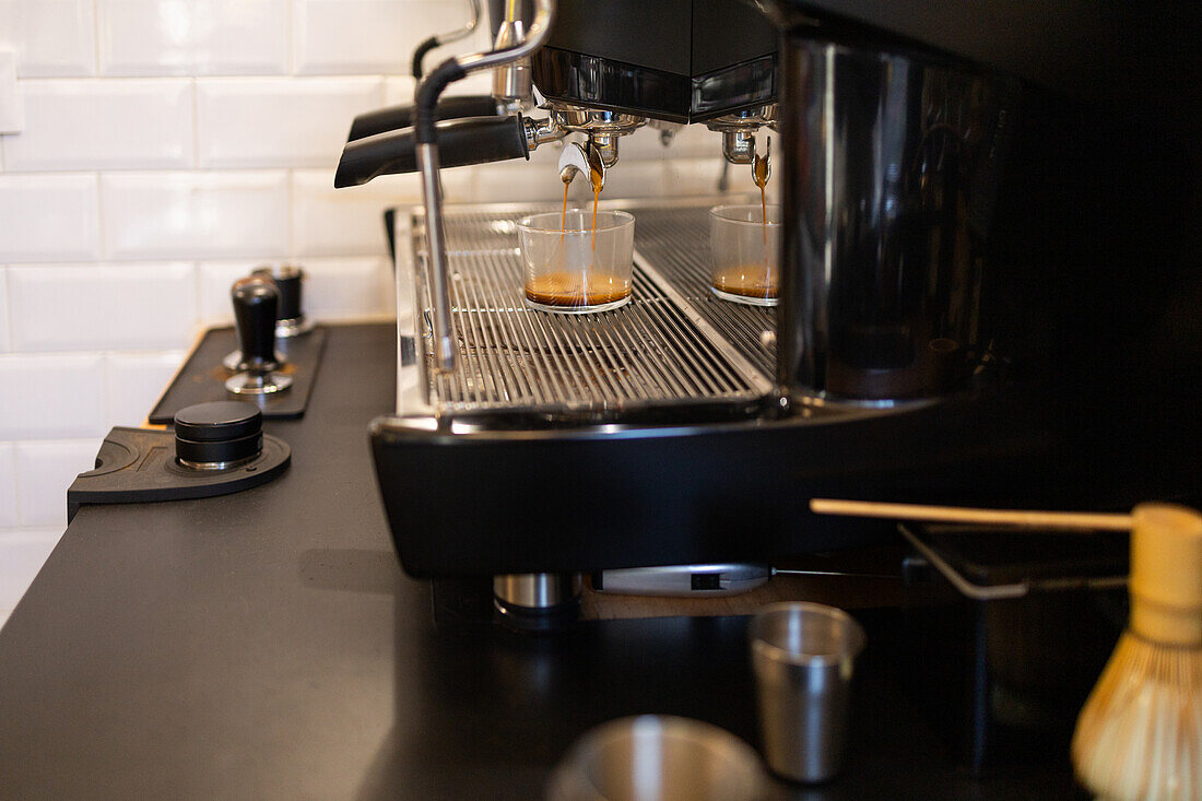 Close-up image of an espresso machine brewing fresh coffee, with the rich espresso flowing into two clear cups on a drip tray.