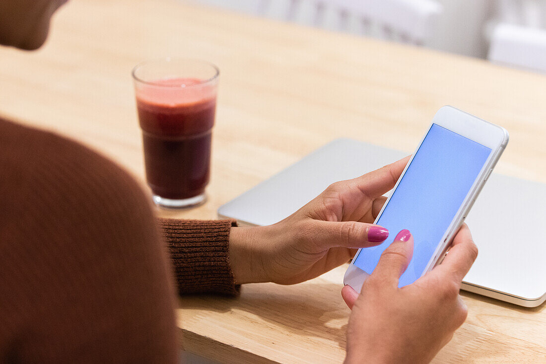 Cropped unrecognizable African American female freelancer browsing smartphone while sitting at table in cafe and working on remote project