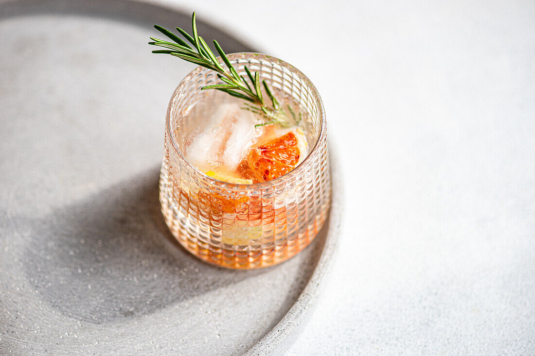 A crafted vodka tonic cocktail adorned with grapefruit and rosemary, resting on a textured tray for an upscale serving experience