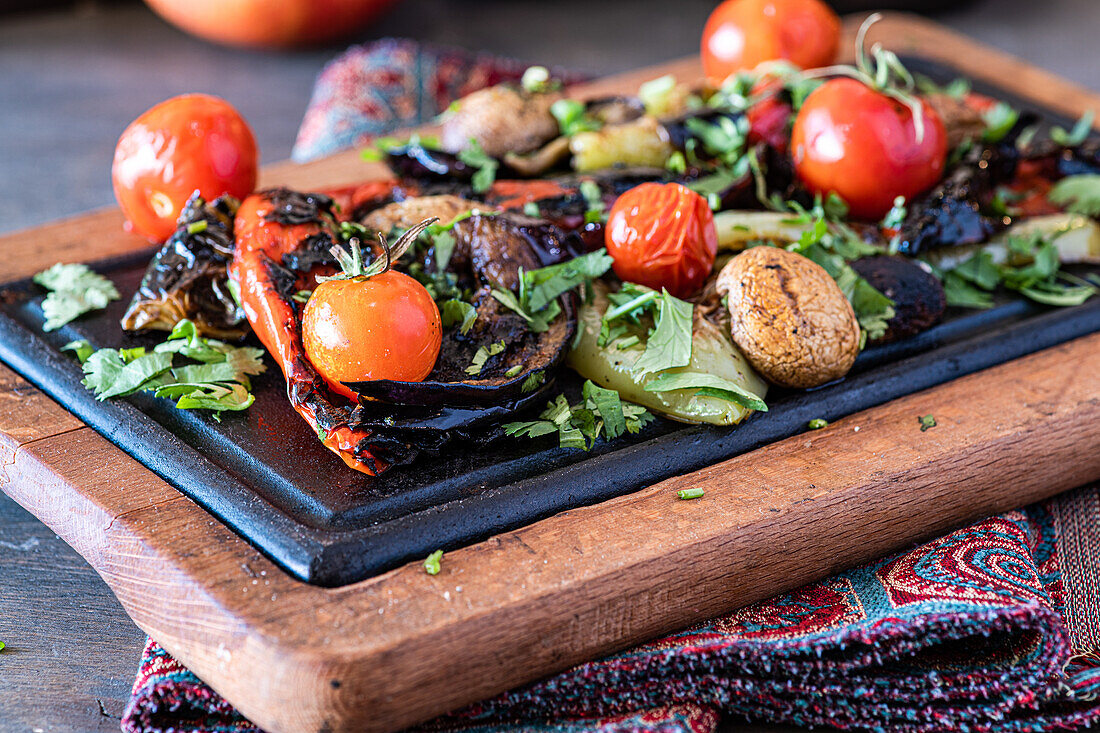 A vibrant display of grilled vegetables including bell peppers, mushrooms, and eggplants, garnished with fresh parsley and served on a dark wooden cutting board